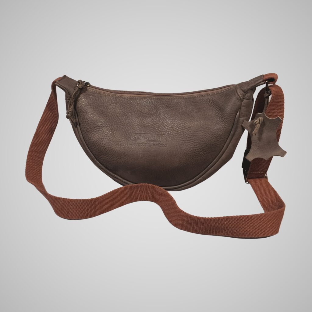 Front view of Lumengin Half Moon cross-body bag in brown hand tipped distressed leather with rust webbing strap, on soft grey