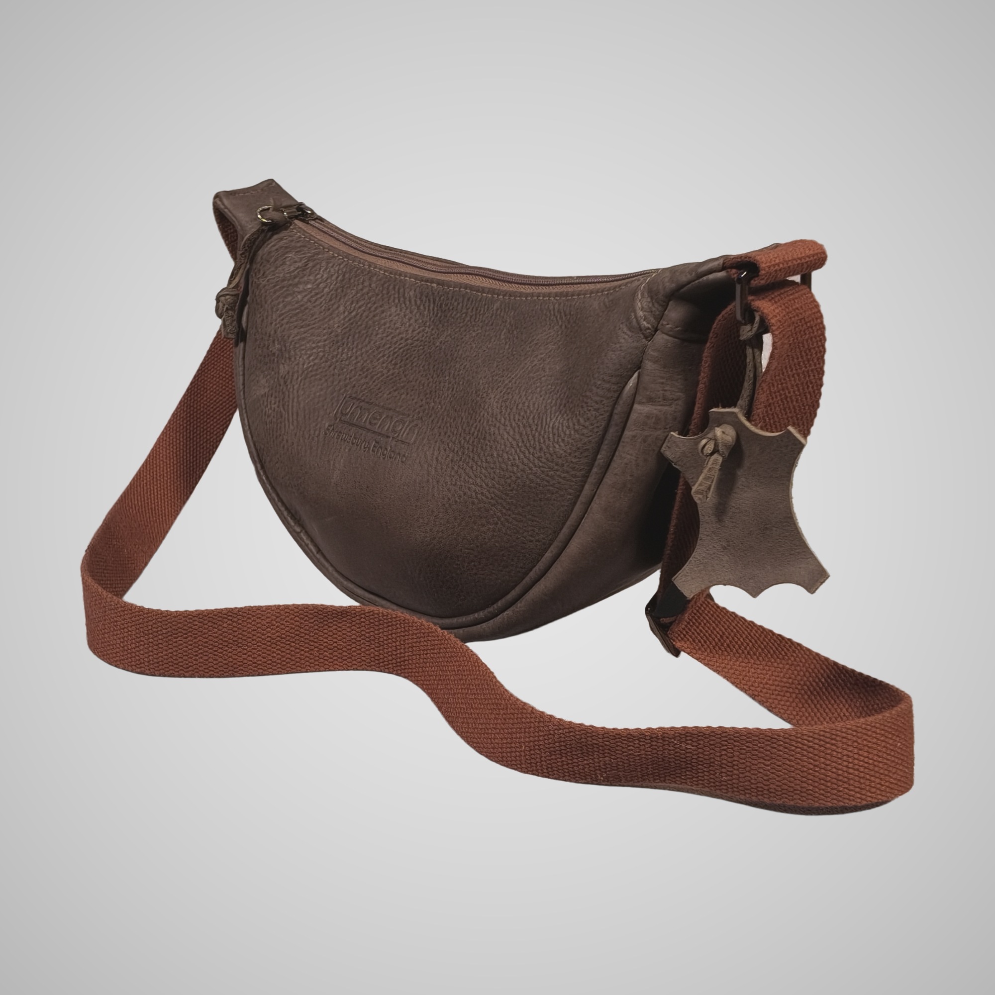 Three-quarter front view of Lumengin Half Moon cross-body bag in brown hand tipped distressed leather with leather hide tag
