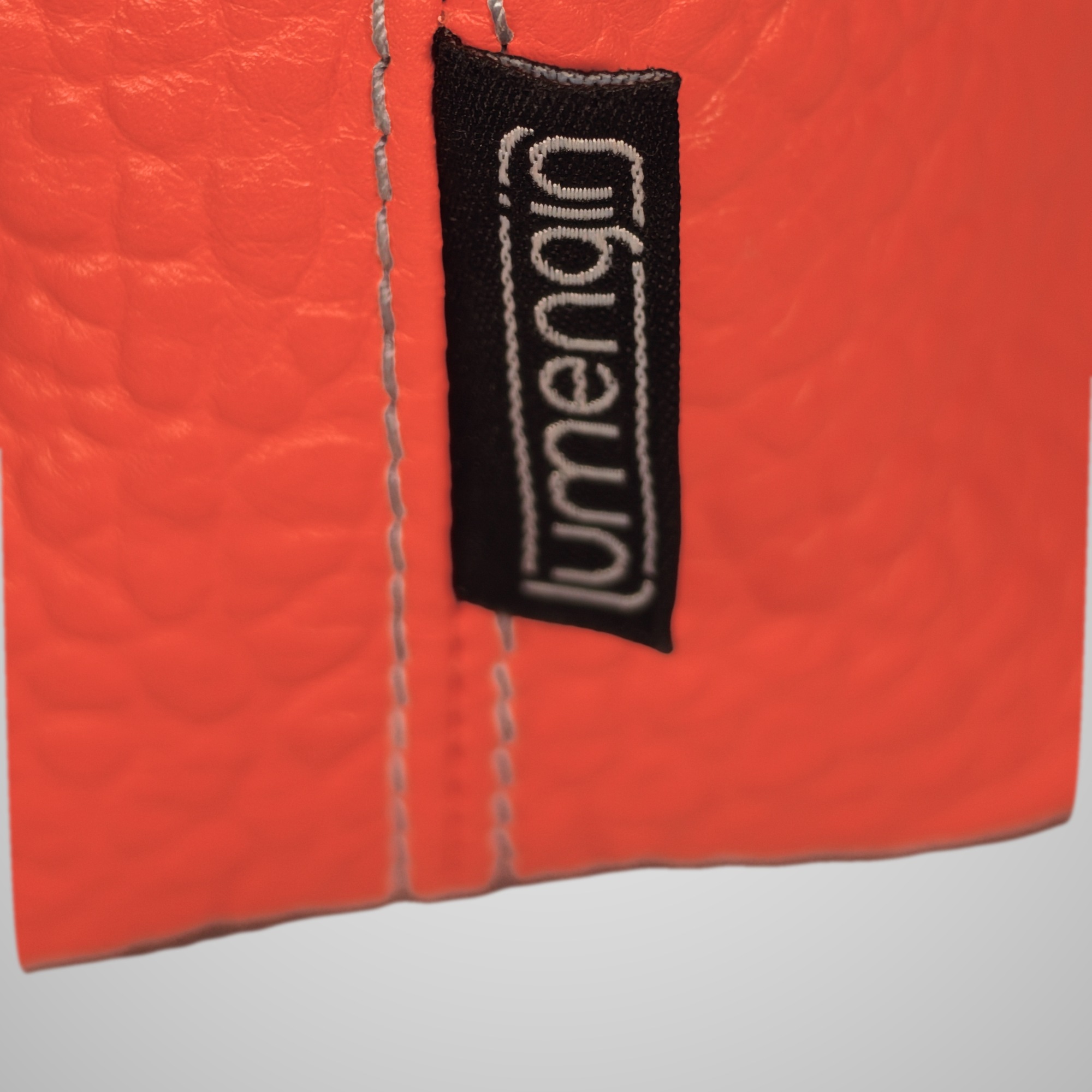 Close-up of the Lumengin label on the bright orange pebbled leather side seam