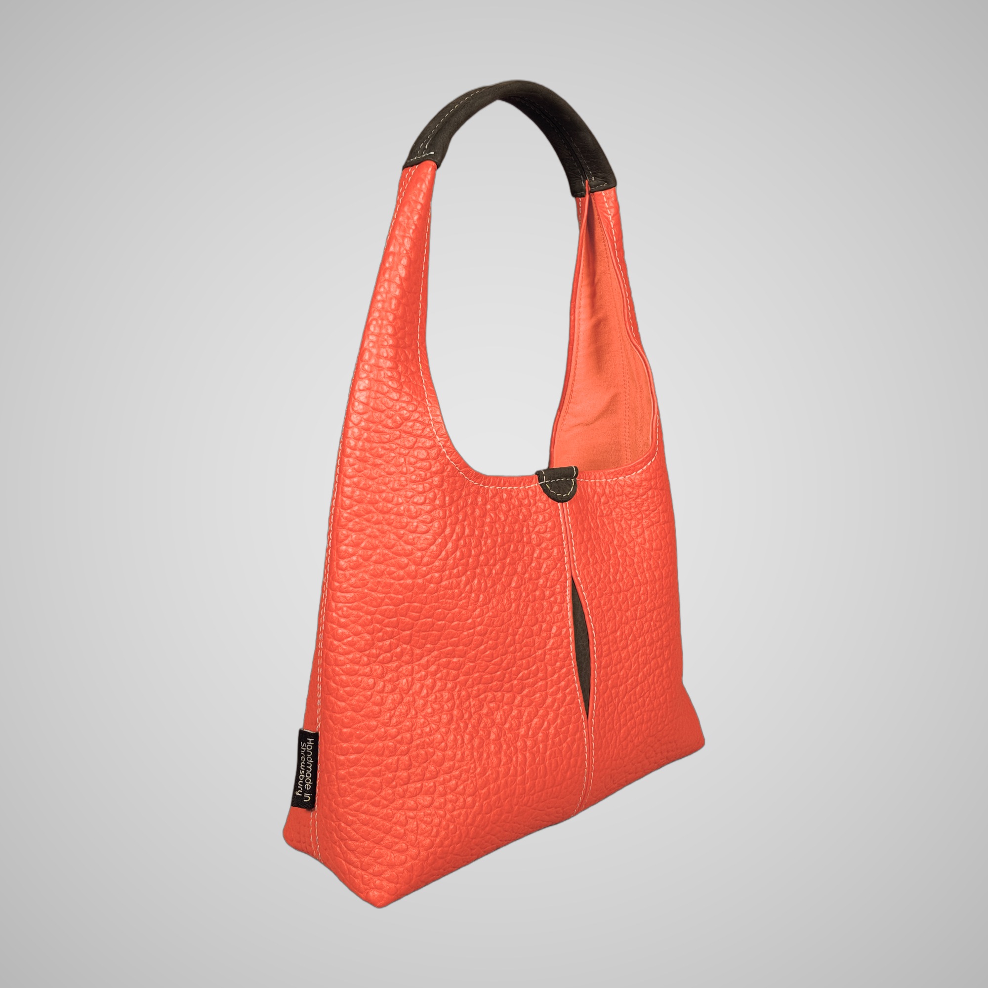 Three-quarter view of Lumengin Bubble Orange medium hobo bag in bright orange pebbled leather showing the orange lining, on soft grey